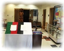 Lobby area of beige walls with lectern draped in a flag of green, red, black, and white. a glass case and a tall wood-carved sculpture in the background