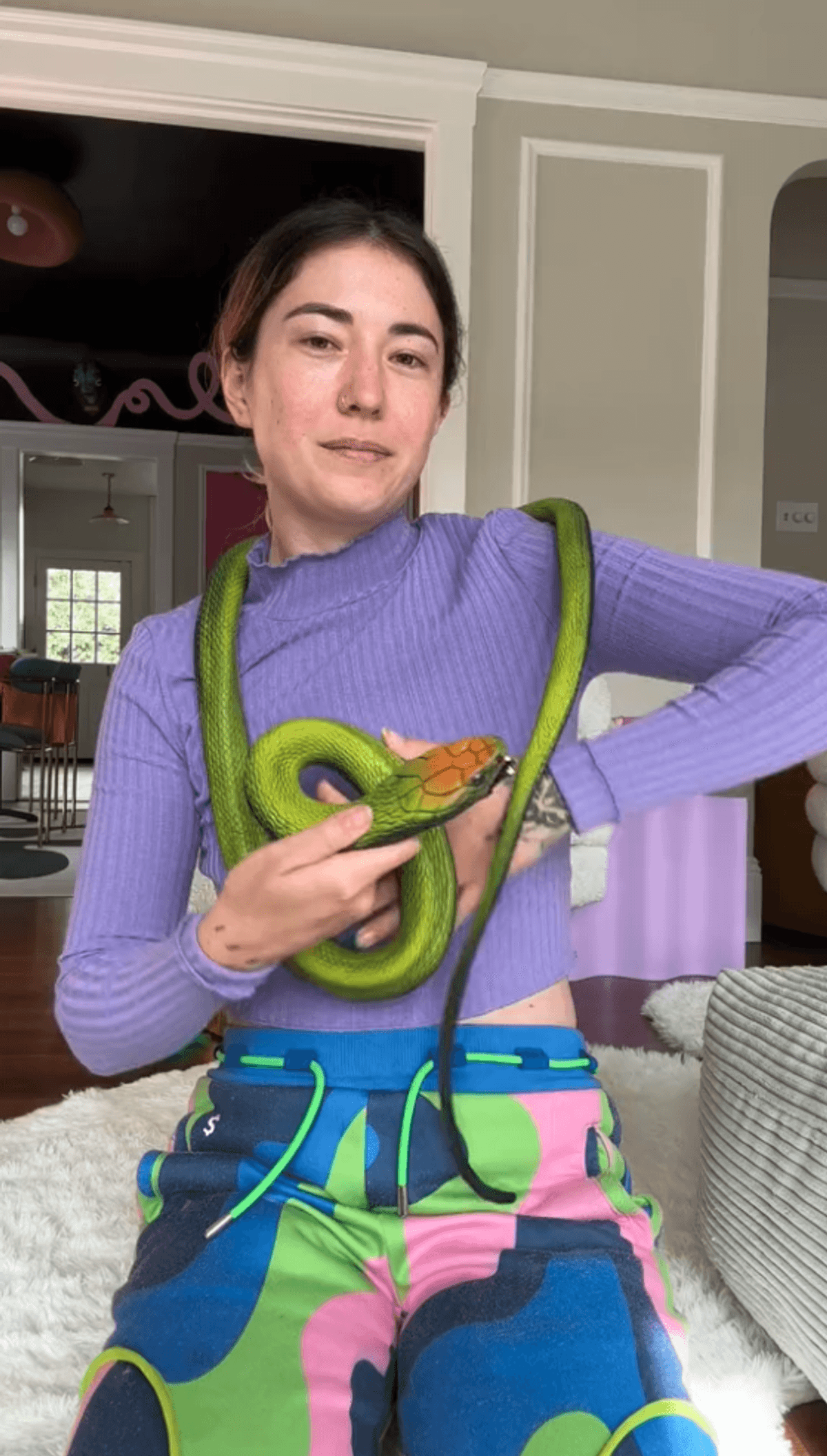 Person sitting with green snake wrapped around shoulders.