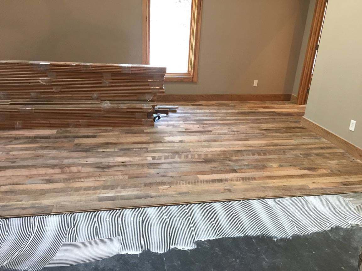 Engineered barnwood flooring from reclaimed wood getting installed.