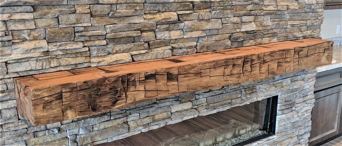 Hand hewn rustic mantel on stone stacked fireplace.