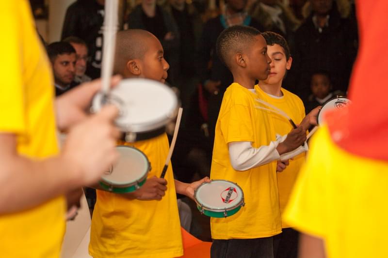 Children wearing yellow t-shirts playing tamborims.