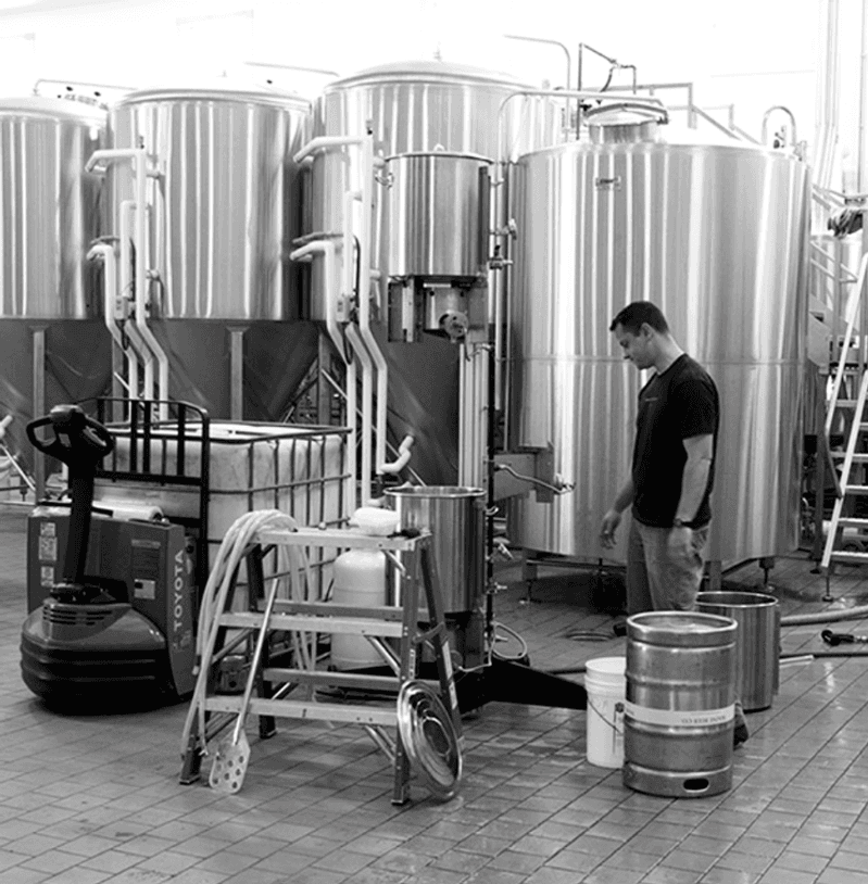 The co-founder of Maine Beer Company, stands in the brewhouse next to stainless steel tanks.