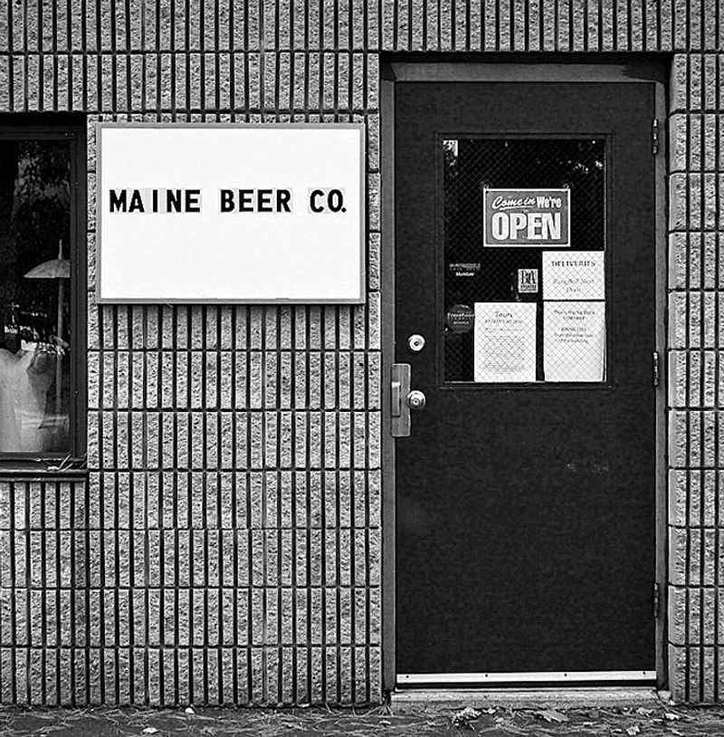 A black and white photo of Maine Beer Company's original location in Portland, with a simple white sign.