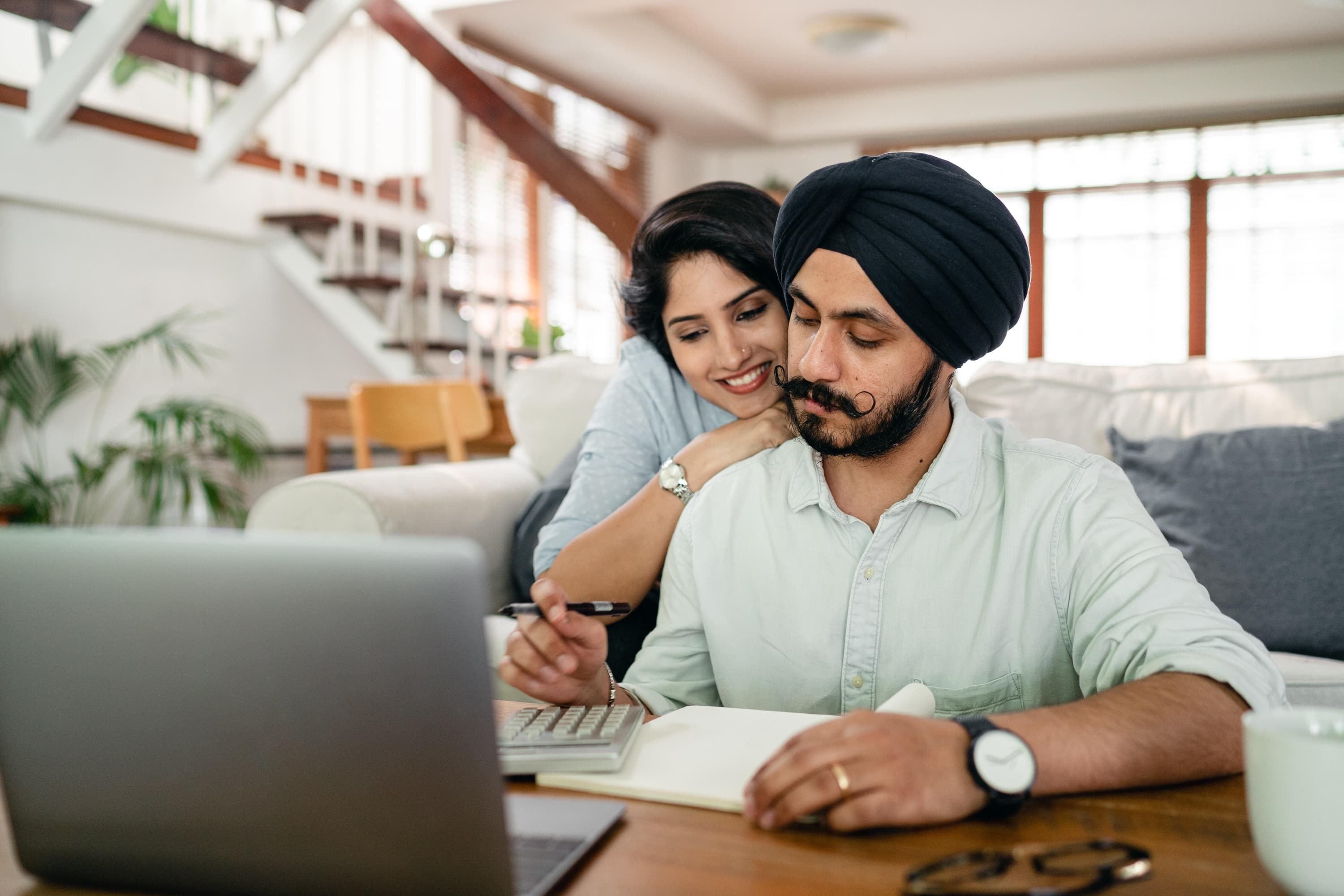 A man and a woman looking over calculations in their house with a pair of glasses and a computer sitting on the table.