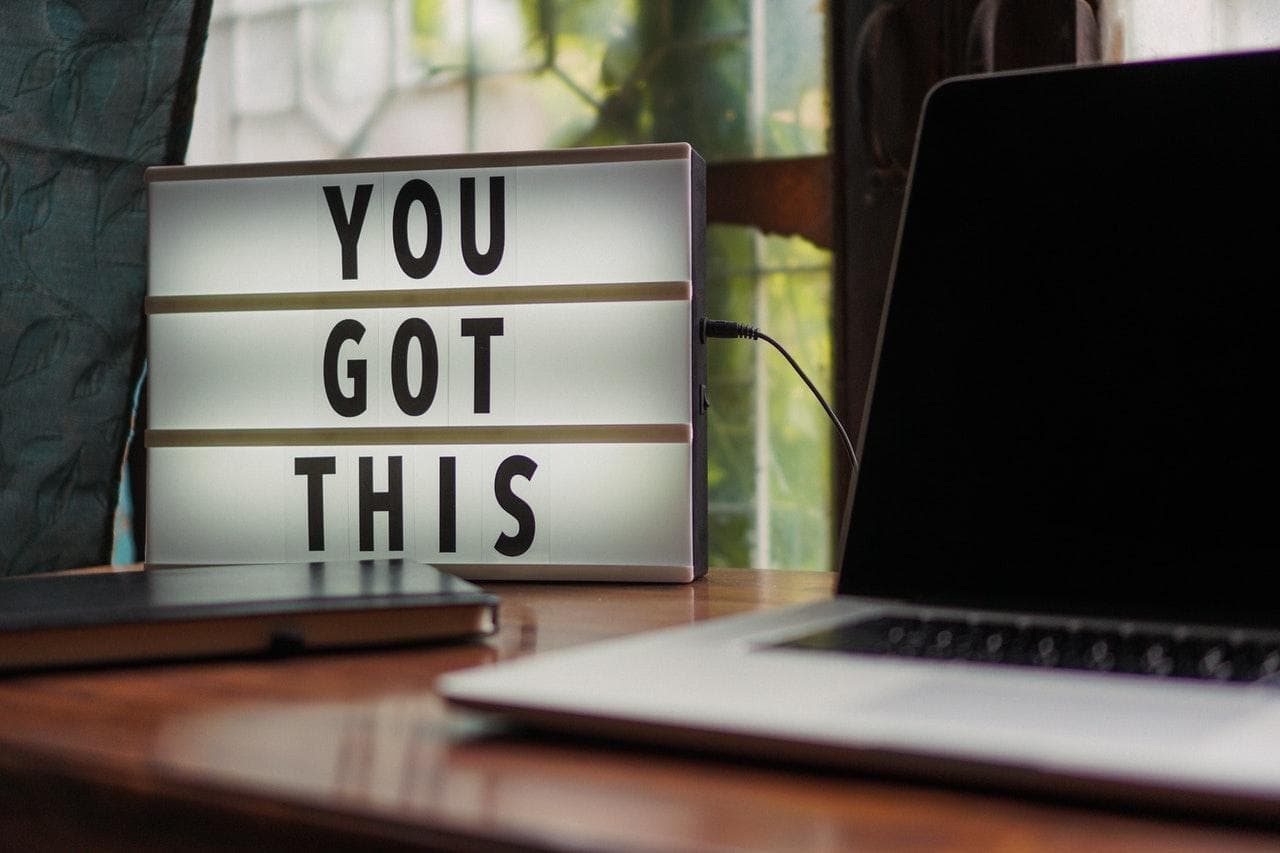 There is a sign set up saying “You Got This” next to an open silver laptop sitting on the desk.