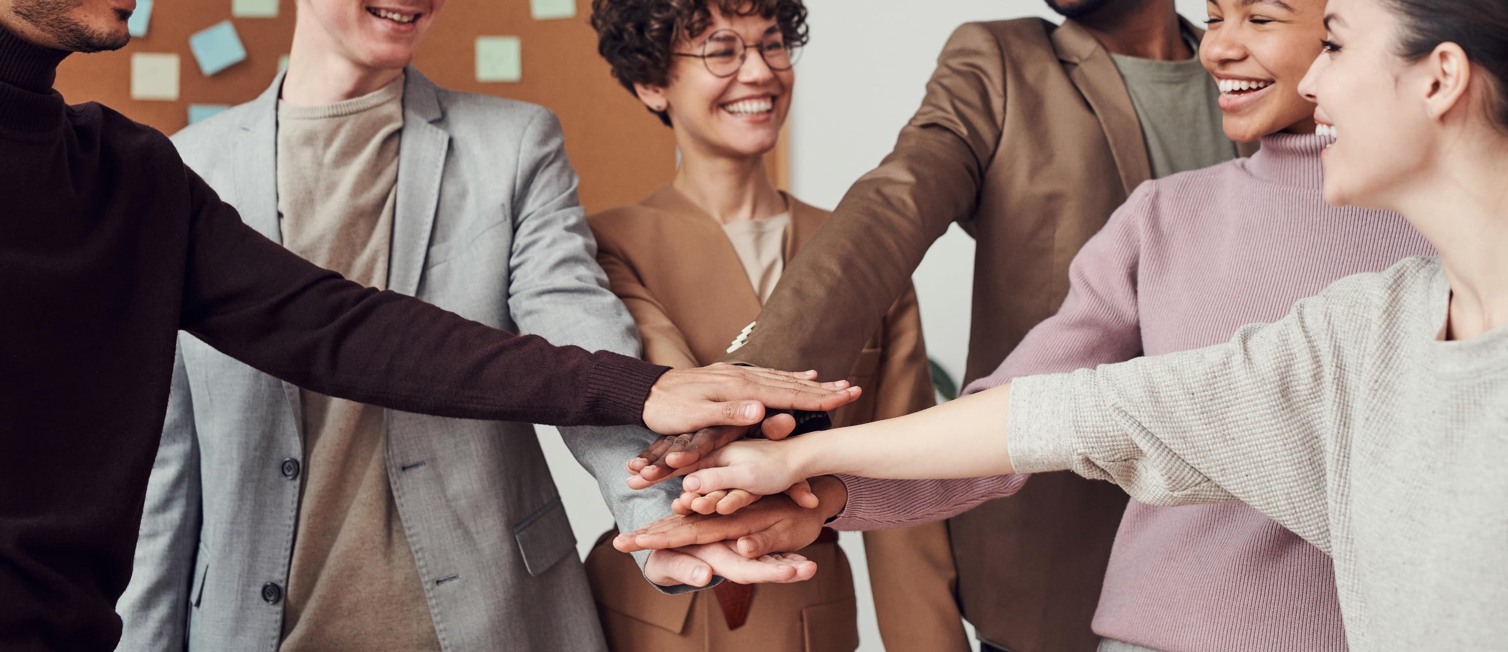 Group of co-workers smiling and putting their hands together, creating a team-like environment.