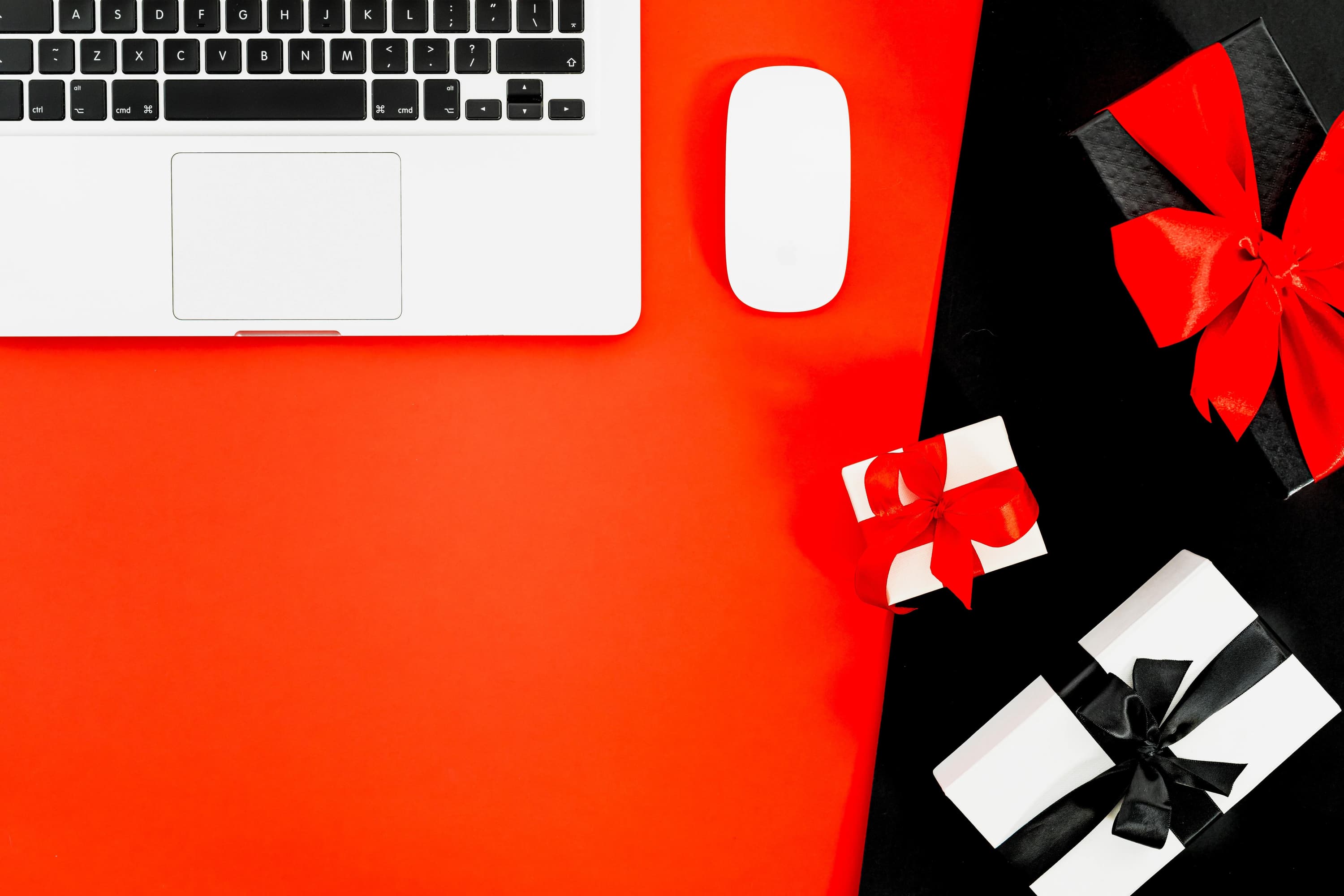 A silver laptop and white mouse and sitting on a table next to three wrapped gifts with bows on them.