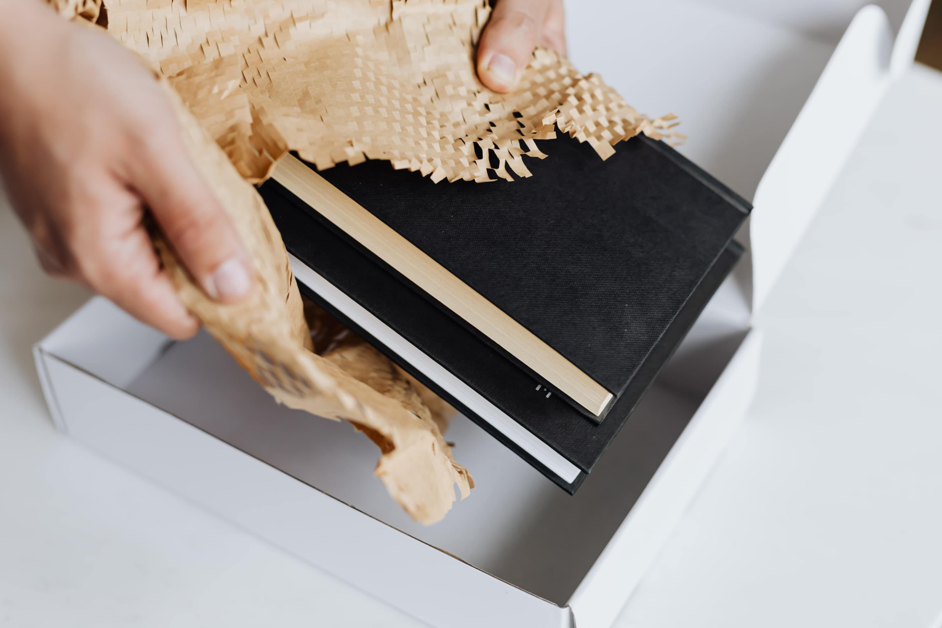 Someone is opening a gift in a white box, pulling out two books with black covers.
