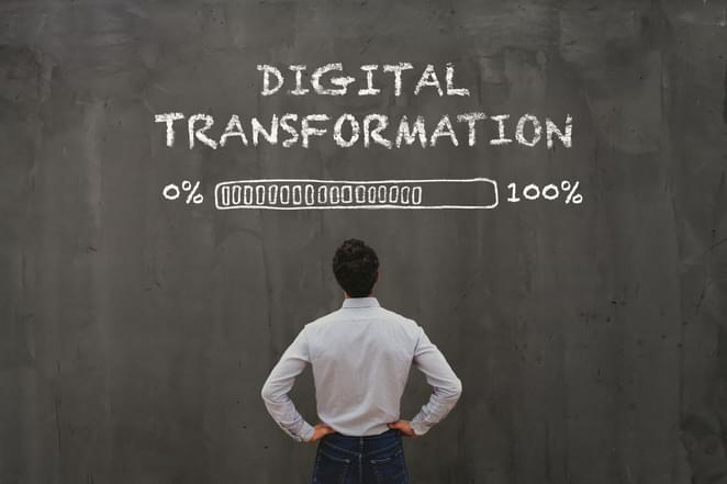 A man is standing before a chalk board that says Digital Transformation that has a loading bar that goes from 1 to 100 and is about 80% full.