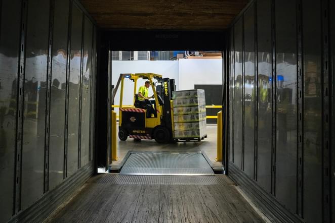 A manufacturing employee is on a forklift getting ready to start loading a container truck for shipment.