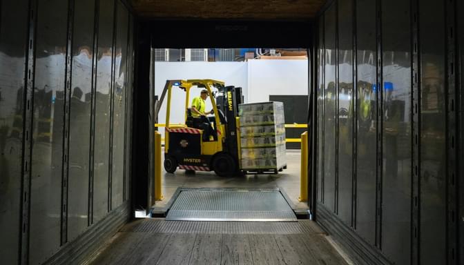 A manufacturing employee is on a forklift getting ready to start loading a container truck for shipment.