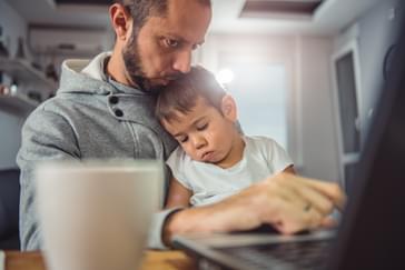 Webinar Recap: How TeamSense Helps HR Communicate with Hourly Workers About Open Enrollment dad typing on the computer with a child asleep on lap