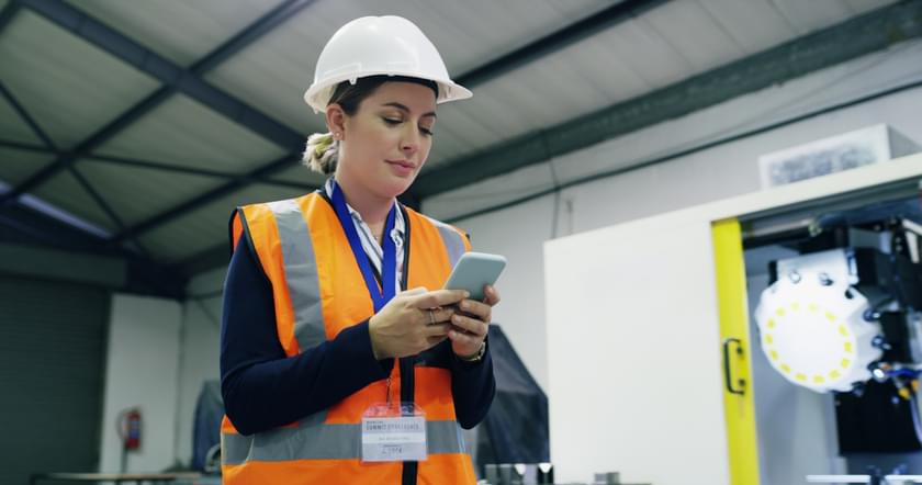 A manufacturing floor manager is on her phone after she received a text alert from and hourly employee