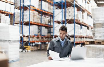 A manufacturing manager is sitting in the warehouse reviewing industry trends and forecasts for 2023.