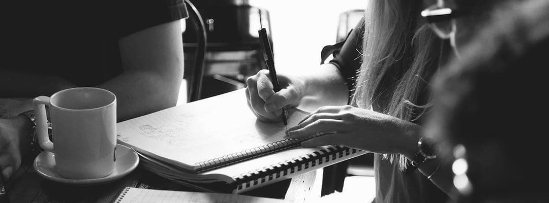 A black and white photo of a girl writing notes in a journal