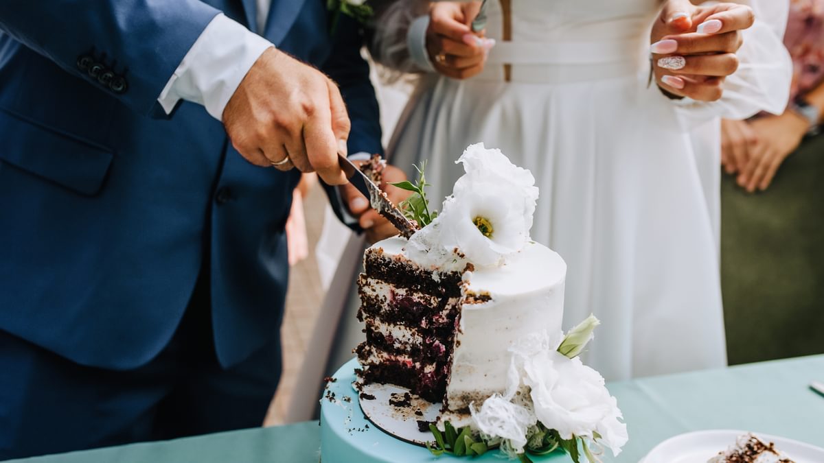 Der Bräutigam und die Braut schneiden die Hochzeitstorte an