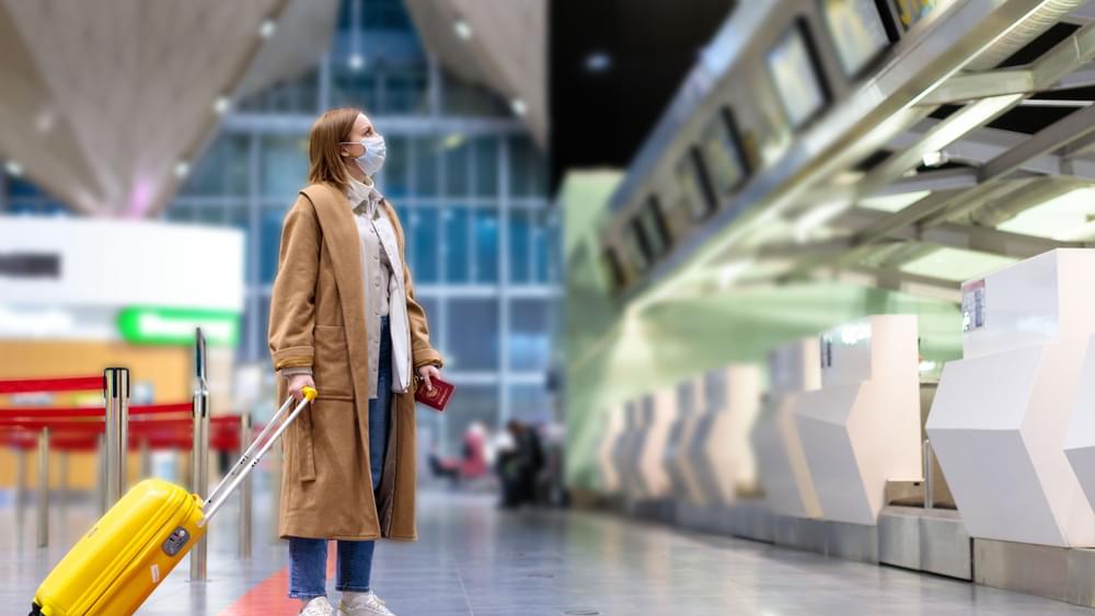 Woman with suitcase standing at empty check-in desks in airport