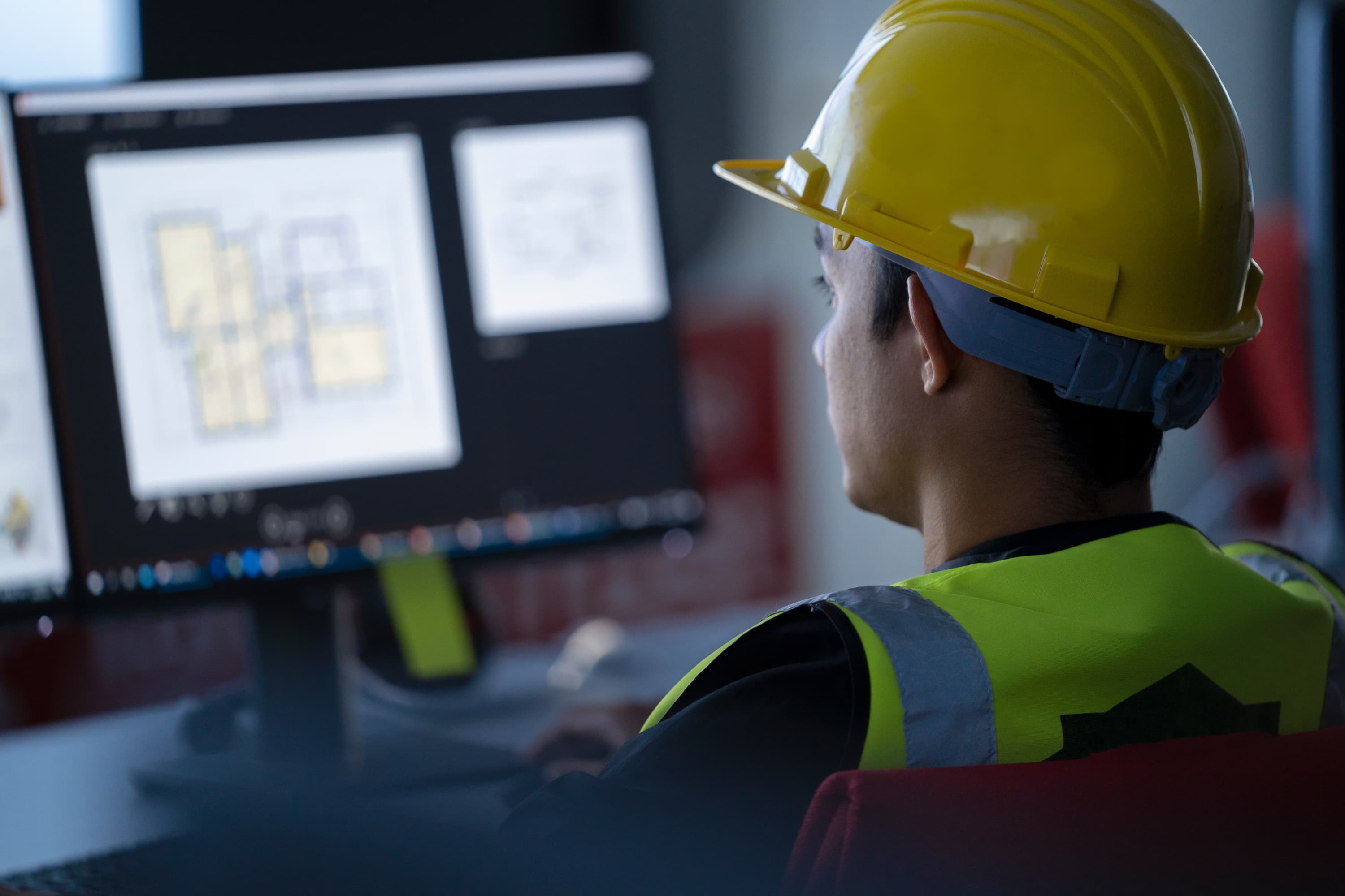 Construction worker in hard hat looking at floor plan on computer screen