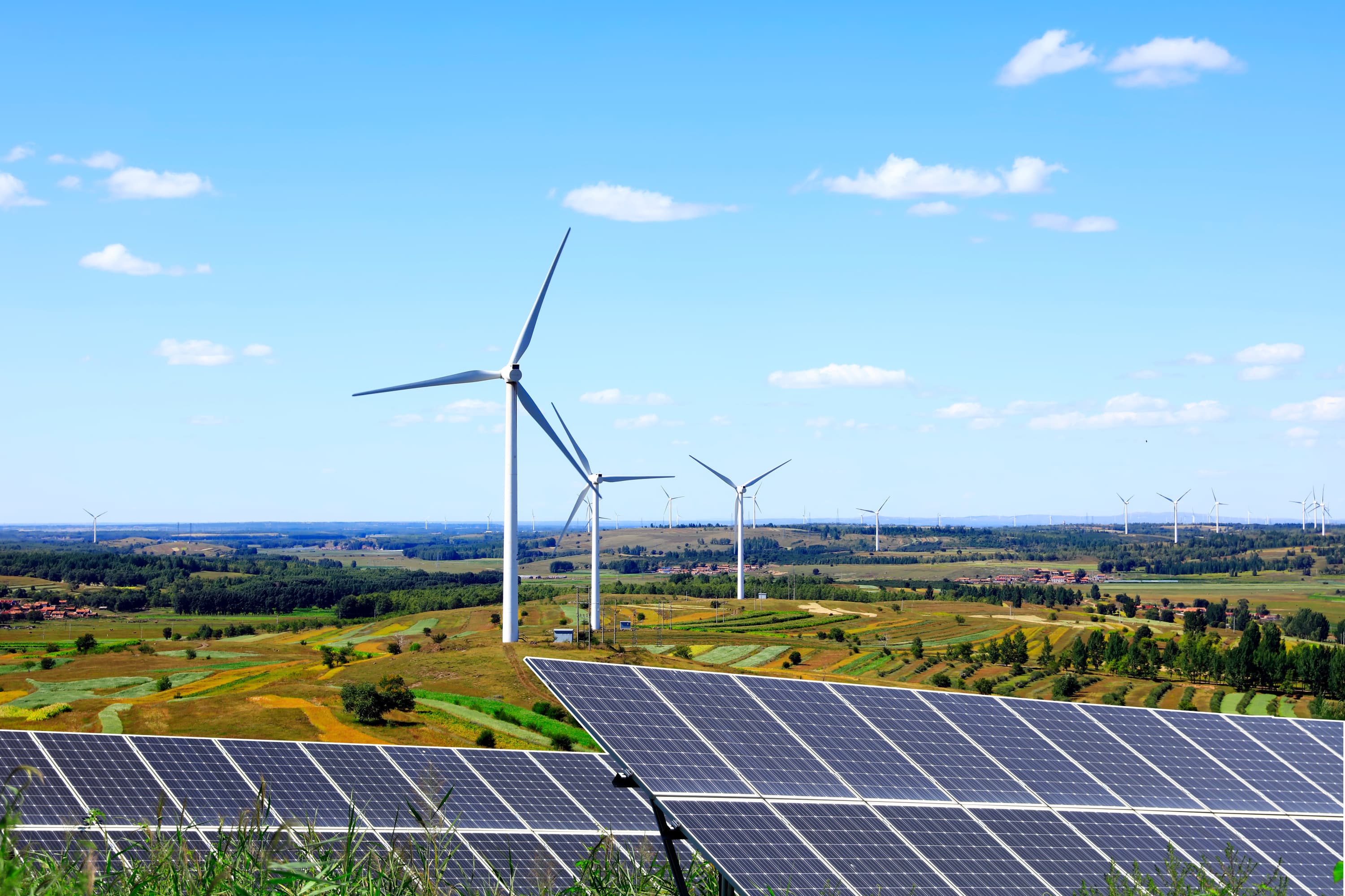 Solar panels with wind turbines in the background