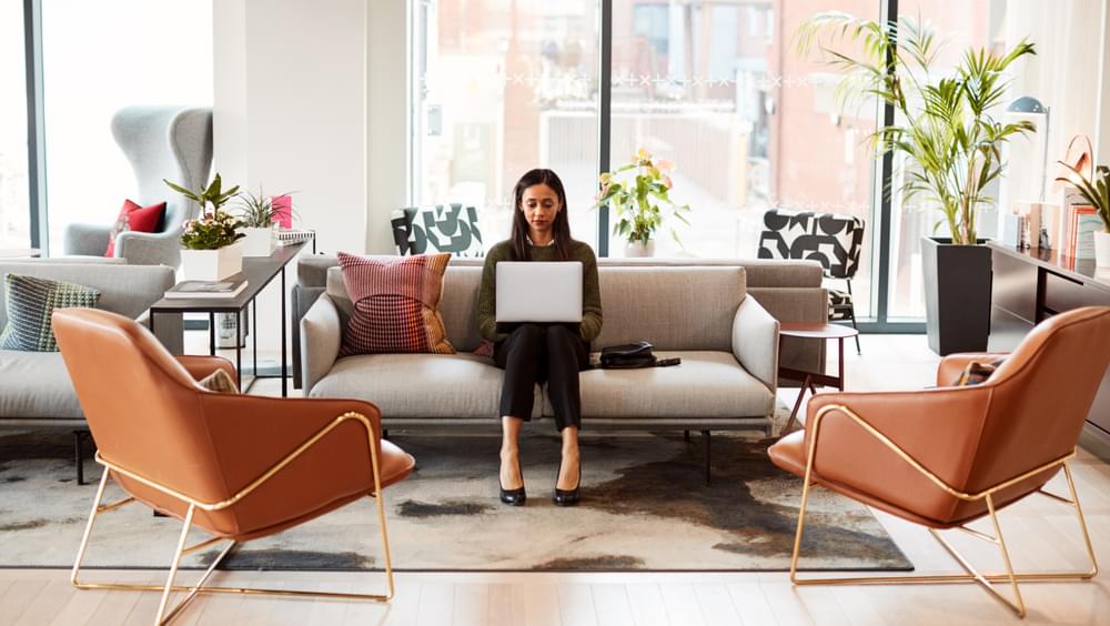 Businesswoman sitting on sofa working on laptop in shared workspace office