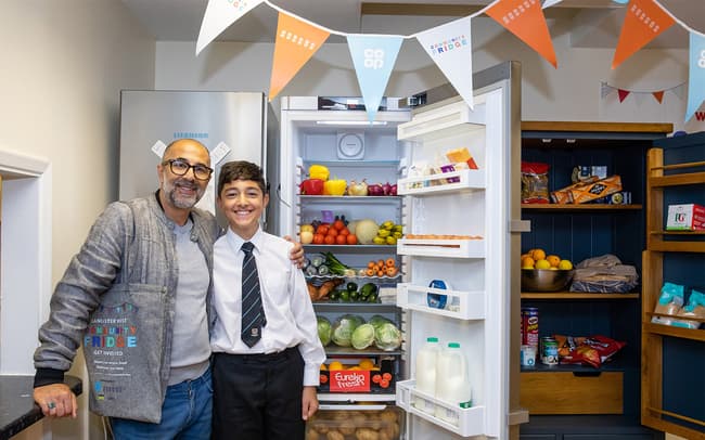 Two people stood next to an open fridge full of food at one of Hubbub's Community Fridges.