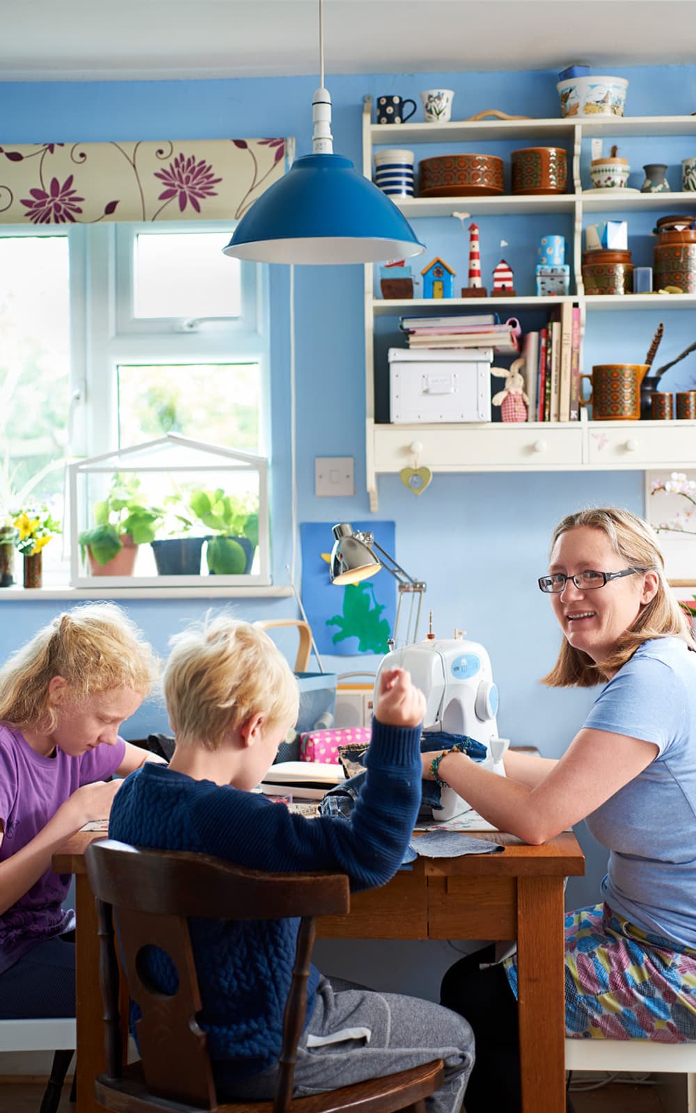 A mum and their two children at home sitting around a table sewing and mending clothes.