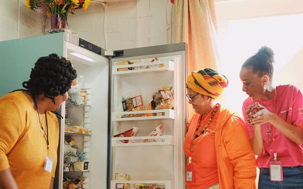 Three people standing next to an open fridge and looking at the food inside.