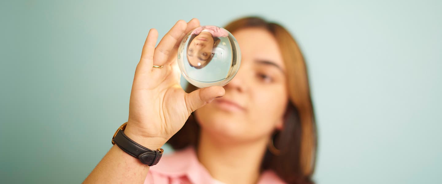 Someone holding up a round glass orb, with their inverted reflection visible through it.