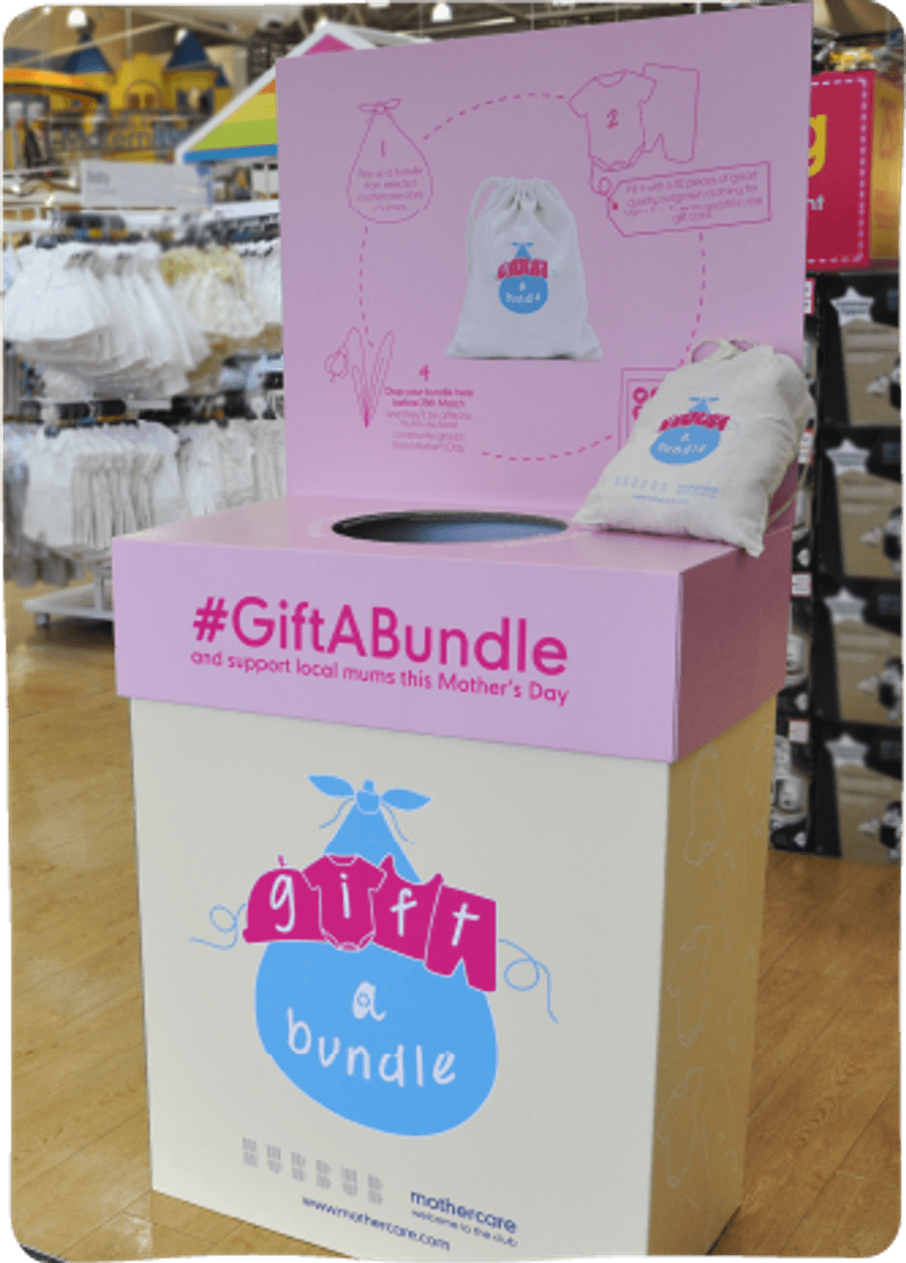 A donation station placed on a shop floor, in the midst of baby clothes. The station's design reads 'Gift a bundle and support local mums this mother's day'