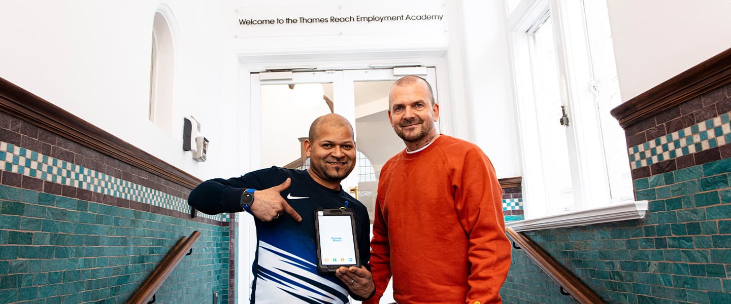 Two people smiling and pointing to a tablet donated to the Tech Lending Community