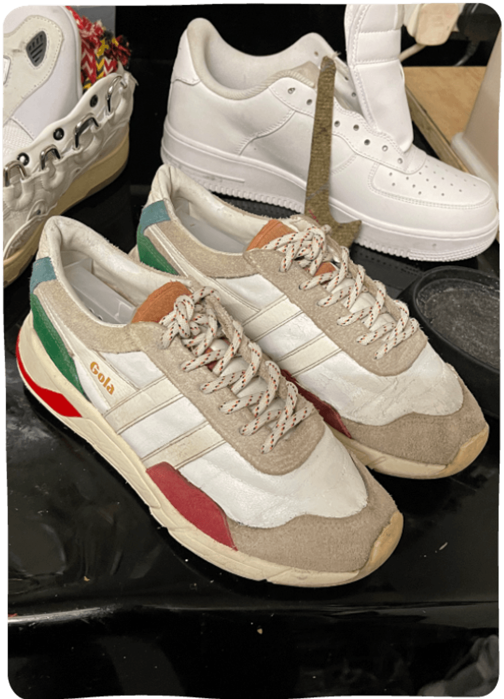 A pair of Gola trainers (white with bright colourful accents) on a workbench. The trainers are visibly not new, but look fresh and well looked after.
