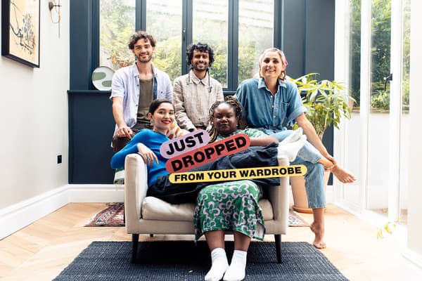 A diverse group of young adults wearing colourful clothes sit on a sofa, smiling at the camera. They hold a sign reading 'Just dropped from your wardrobe'