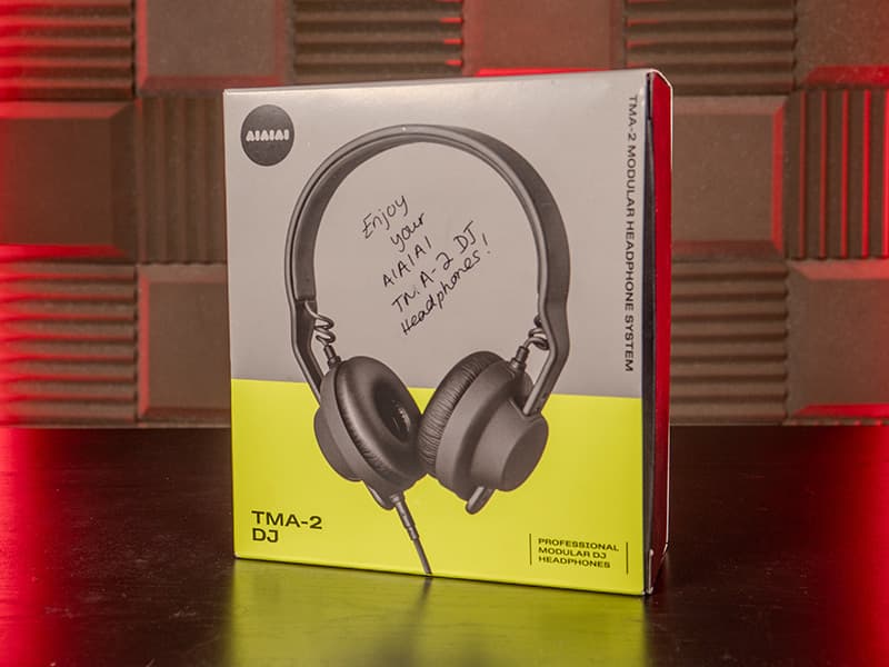 The box of the AIAIAI TMA-2 DJ headphones, stood upright on a desk. The image has red lighting on both the left and right side.