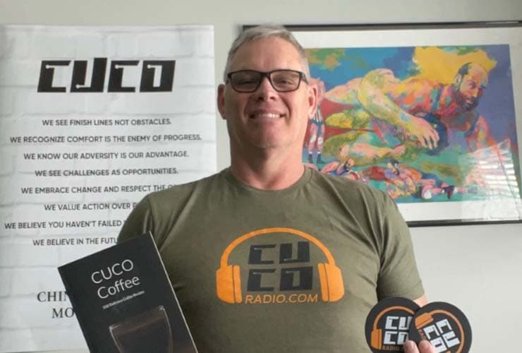 A male CUCO fan holding CUCO merchandise and standing in front of a poster of the CUCO brand values.
