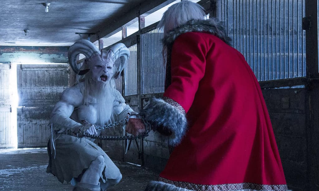A white demon with horns and muscles, looking like the devil, lunges and hisses at Santa Clause in a scary pose. Santa Claus' back is to the camera and he wears a big red fur coat with white sleeves.