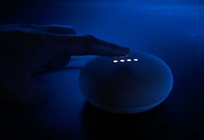 Image shows someone controlling the Google Nest Mini smart speaker by tapping the top of it with their finger.