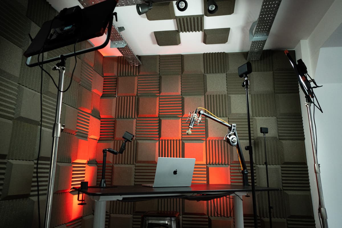 A sound proofed studio showing a laptop on the table, 3 Mevo cameras arranged around it and some professional lights.