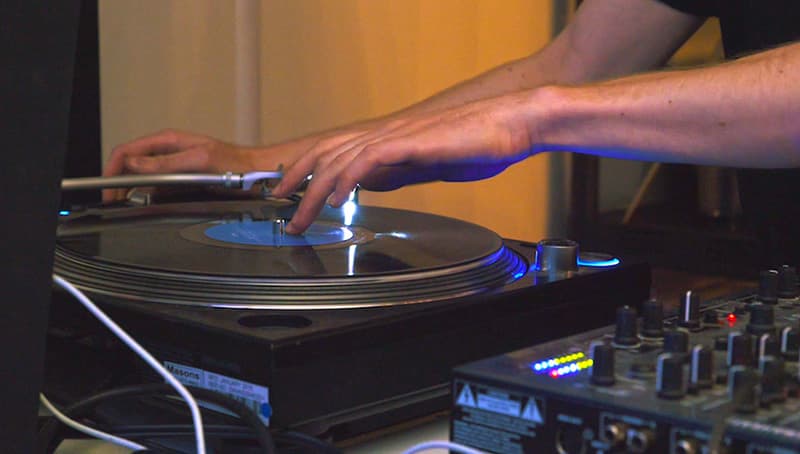 A man DJing with a record, by touching the centre of the record and the pitch control.