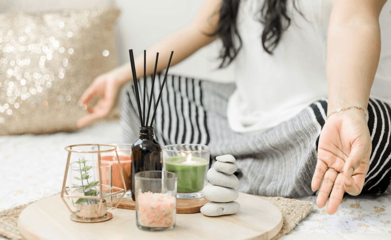 A woman mediates in a 'zen' position in front of a table of candles and incense burners.