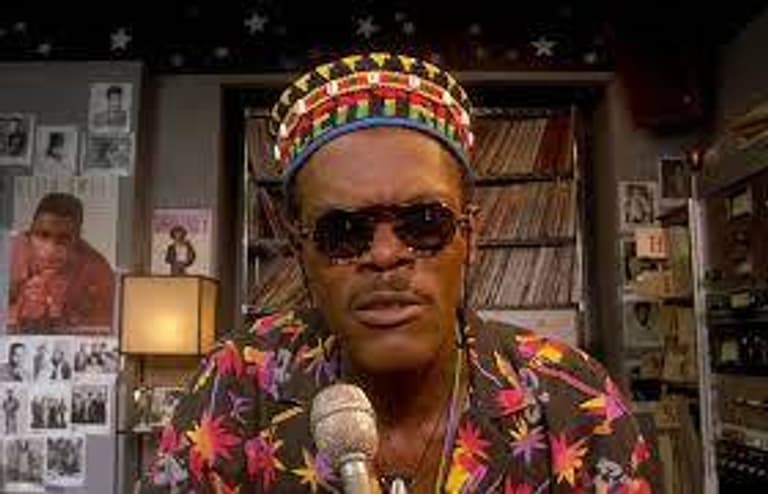 Image shows a still from Do The Right Thing. DJ Mister Senor Love Daddy (played by Samuel L Jackson) is looking straight into the camera, whilst talking in to the microphone.