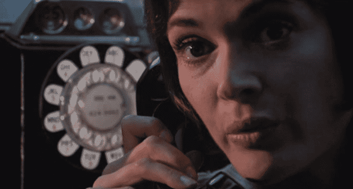 Jessica Walter, a white woman with brown hair and brown eyes, is looking at the camera with her mouth pursed. She is on the telephone, a vintage phone, to Clint Eastwood in the image.