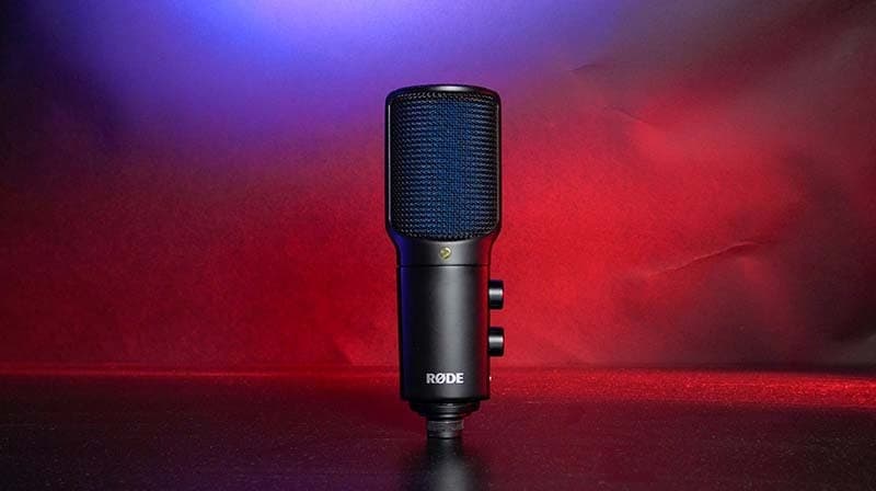 The RODE NT-USB+ mic, positioned upright on a table. Illuminated with red and blue lights.