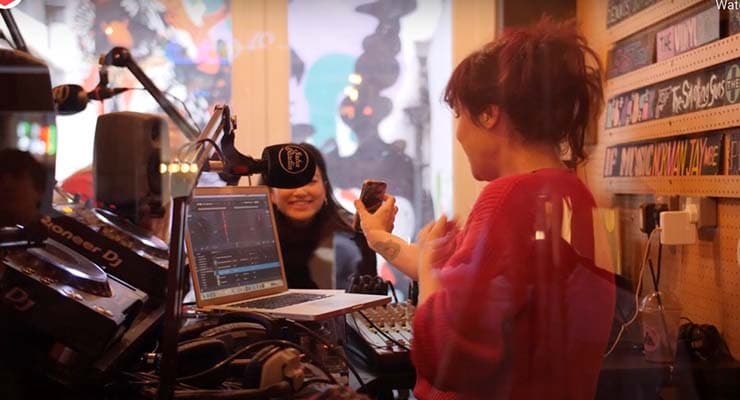 A woman in an open radio booth, showing something on her phone to another woman who is smiling.