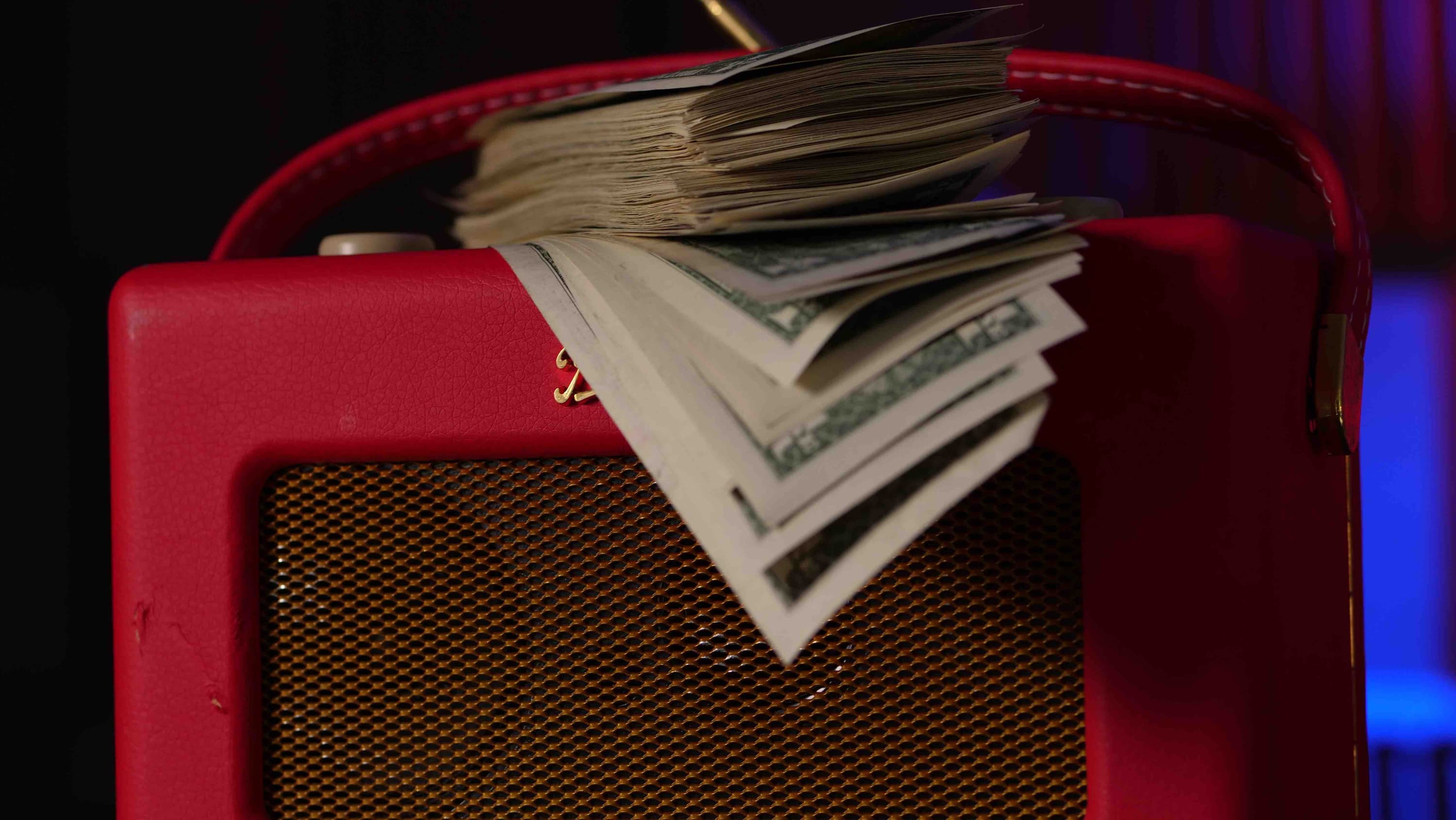 Image shows a stack of dollar bills on top of a red Roberts radio.