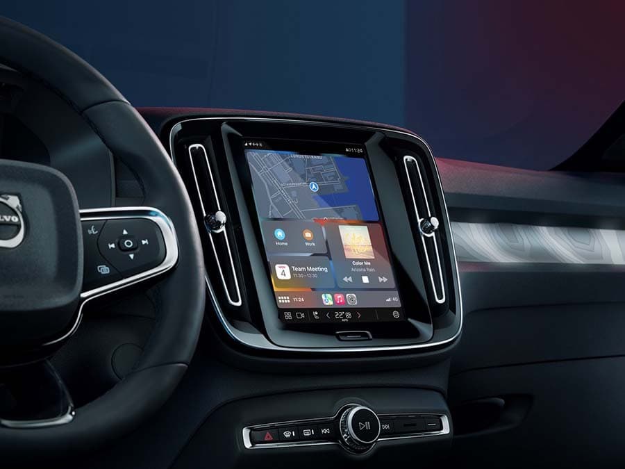 Image shows the interior of a Volvo car. The right half of a steering wheel with the car's infotainment display directly to the right of it.