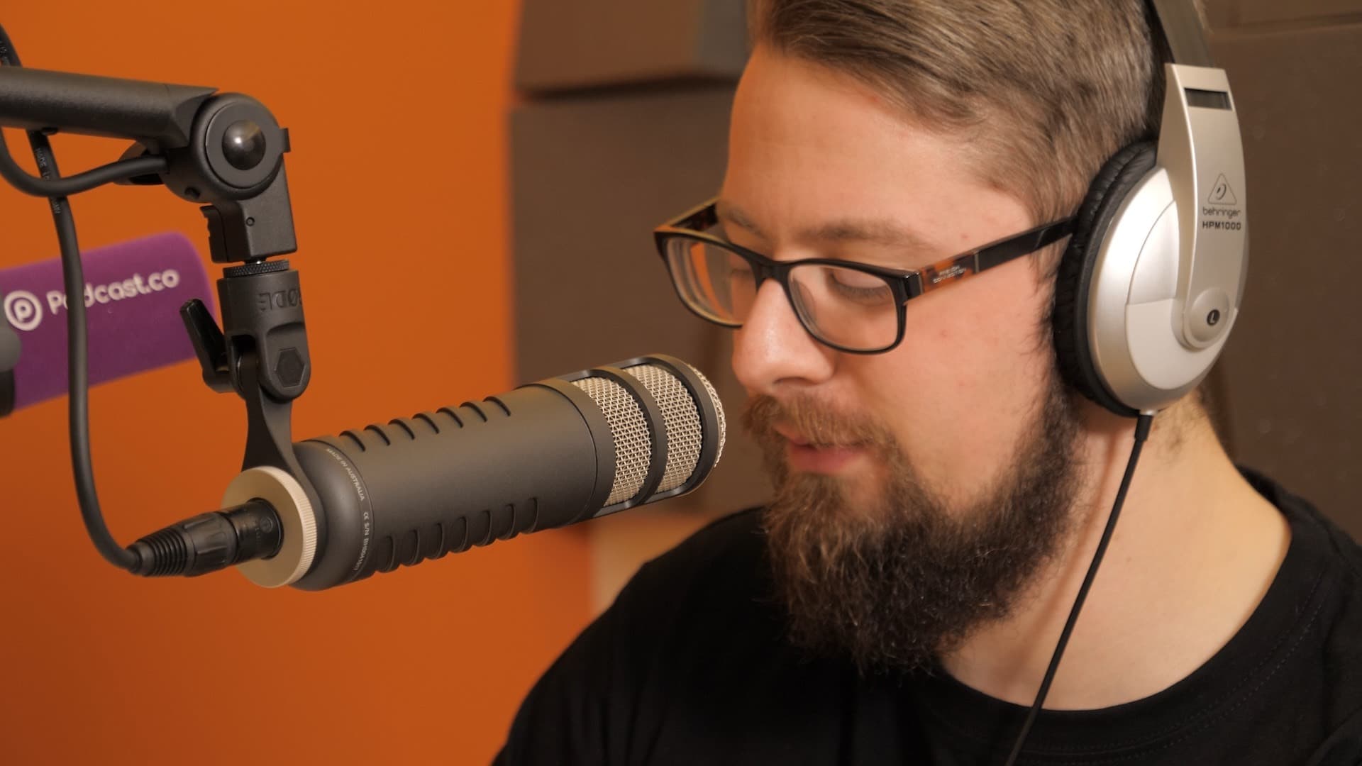 A man wearing headphones and speaking in to a studio microphone.
