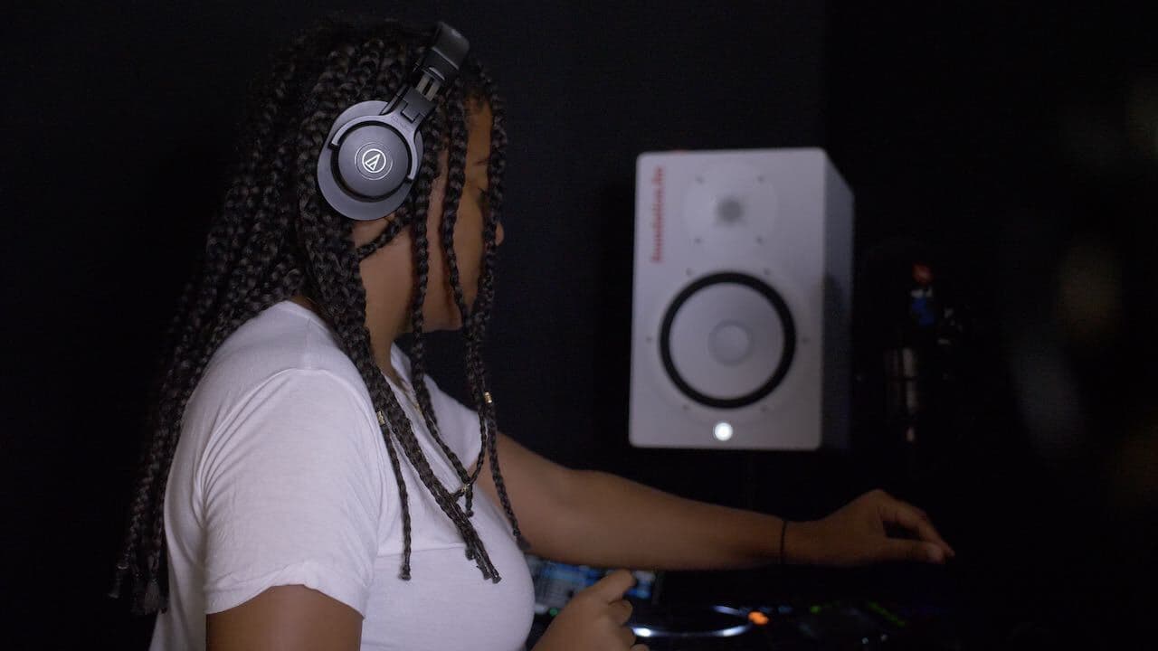 A black woman with braids DJing in a radio booth.