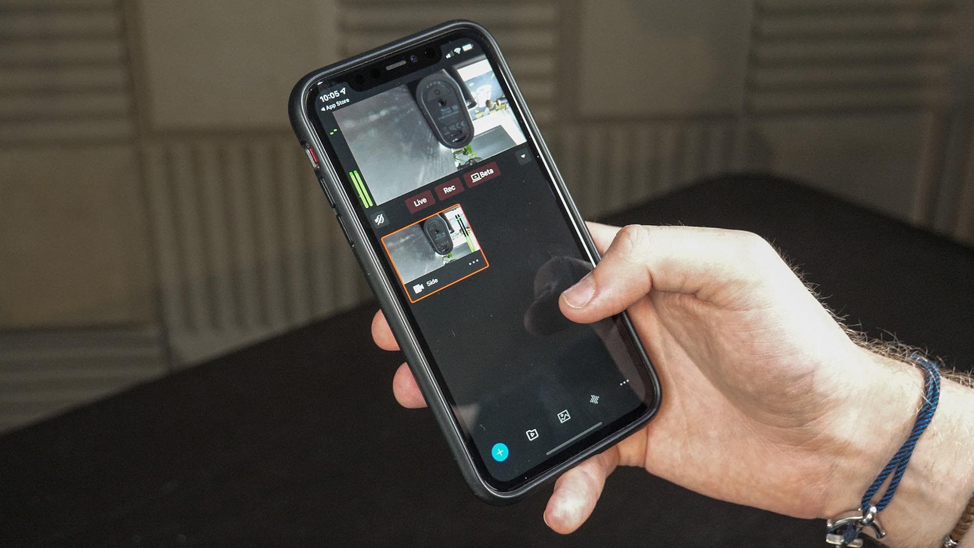 A hand holding an iPhone with the Mevo Multicam app open and showing two camera feeds.