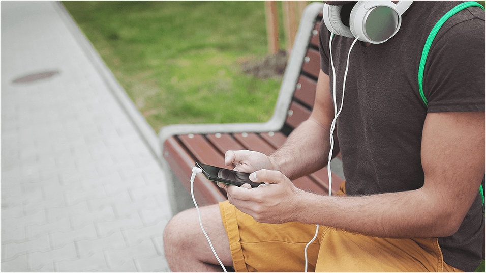 A muscular man sat on a park bench, selecting music on his smartphone.