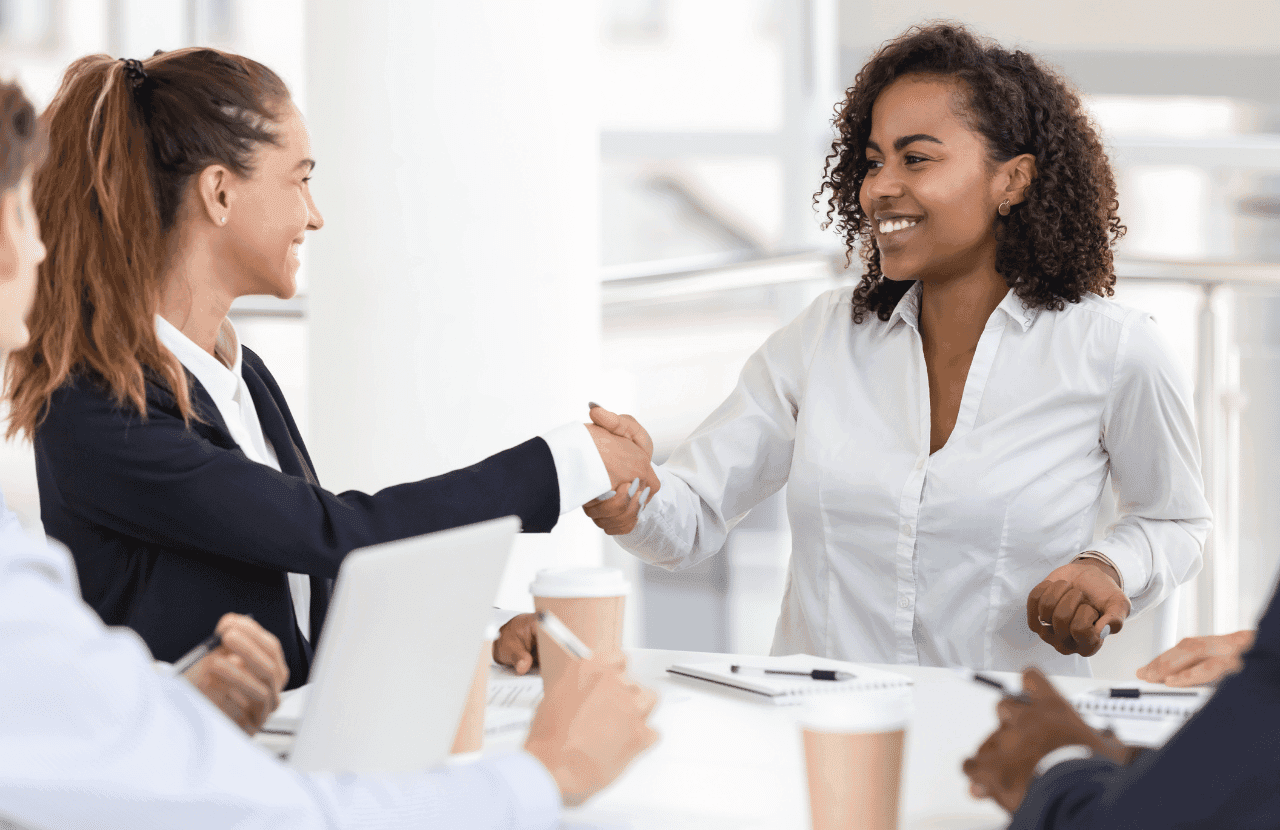 Happy young attractive black woman handshaking with white businesswoman